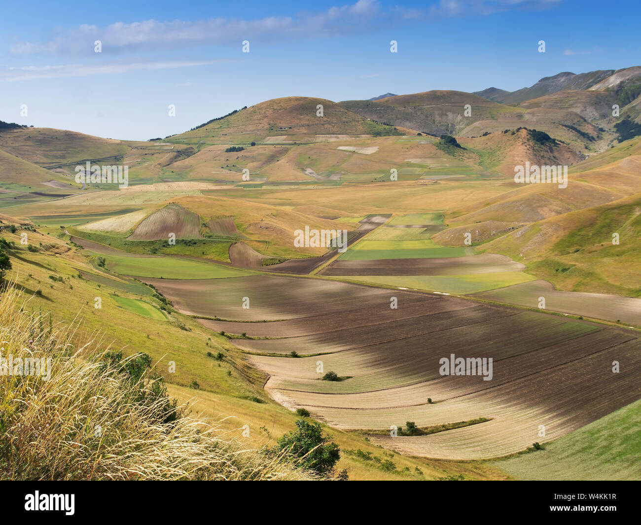 Vista generale della valle, a Castelluccio di Norcia in Umbria, Italia. Campi e colline, con ombre di passare nubi. Paesaggio colorato. Foto Stock