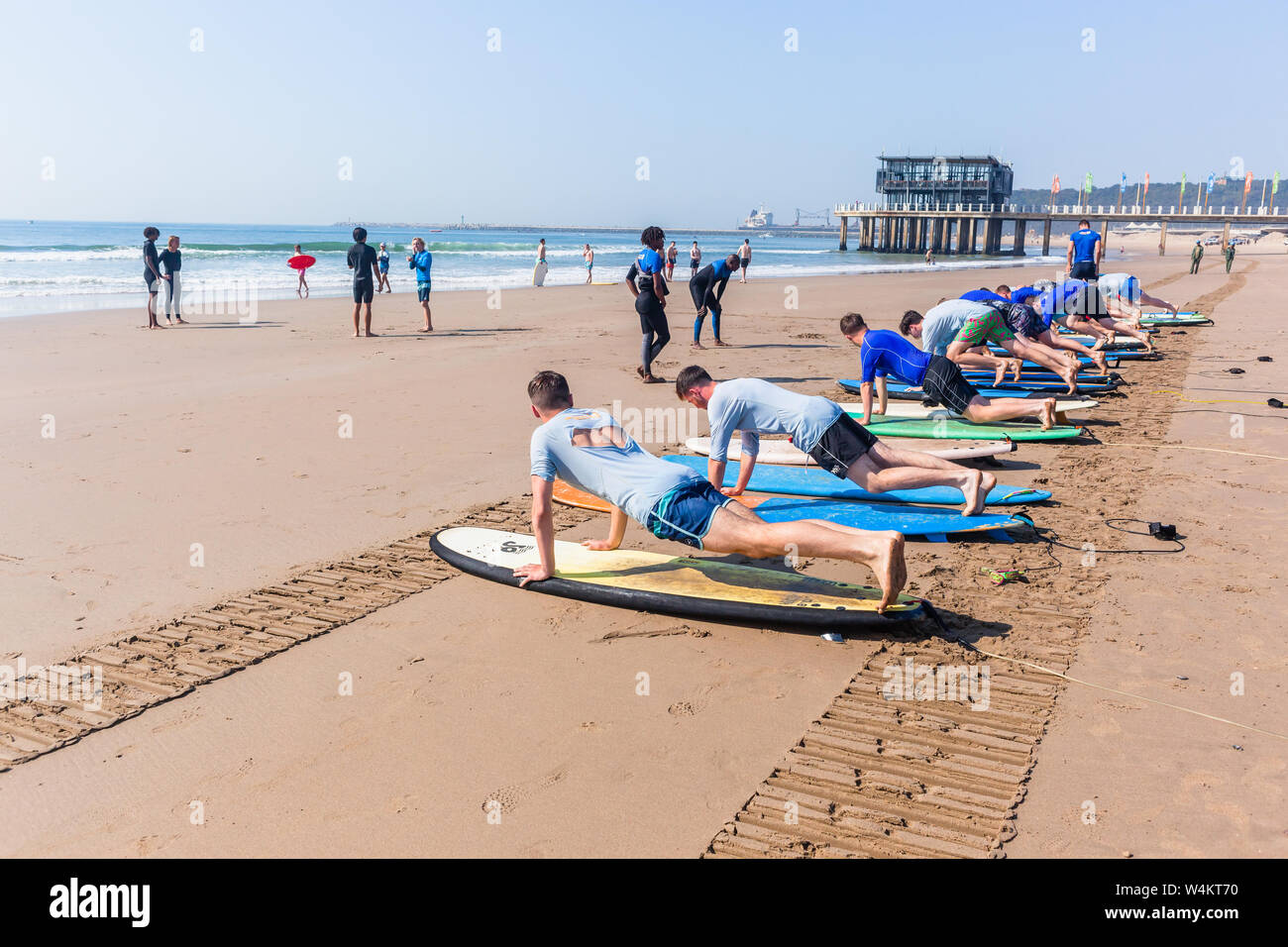 Lezioni di surf sulla spiaggia con tavole da surf con giovani uomini e istruttori di surf sulla base di wave riding skill accanto all'acqua dell'oceano litorale. Foto Stock