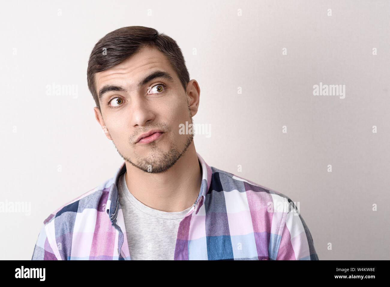 Ritratto di un attraente uomo bianco con un'espressione ambigua su uno sfondo grigio con spazio di copia Foto Stock