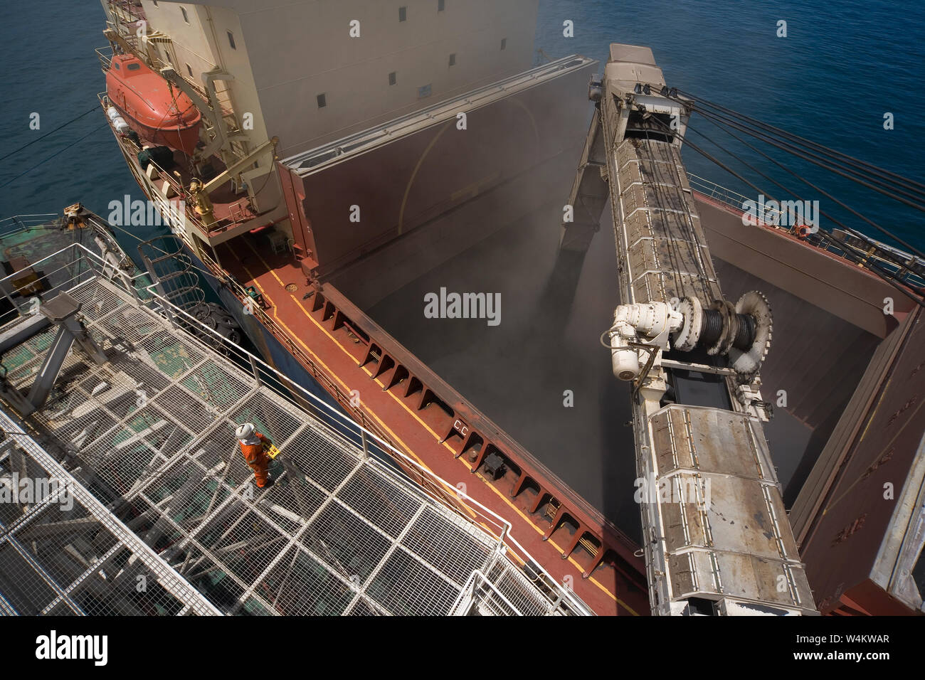 Estrazione, gestione e trasporto di sabbie minerali di titanio. Caricamento di sabbie minerali tramite il braccio di trasporto della chiatta nella stiva del portarinfuse in mare. Foto Stock