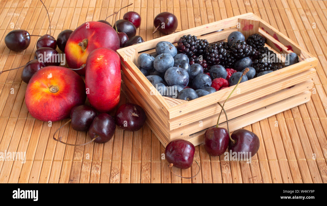 Vita tranquilla con frutte. Lamponi, ciliegie, mirtilli, more e pesche noci piatto. In una piccola cassa di un tappetino. Foto Stock