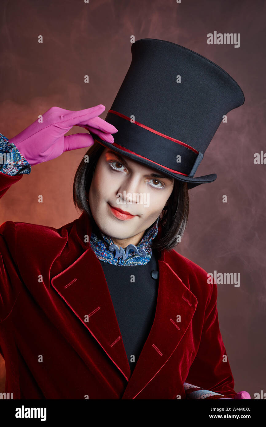 Favoloso circus uomo in un cappello e un abito rosso in posa il fumo su un colore di sfondo scuro. Un clown in un party, uomo gentleman da una fiaba. Wiz Foto Stock