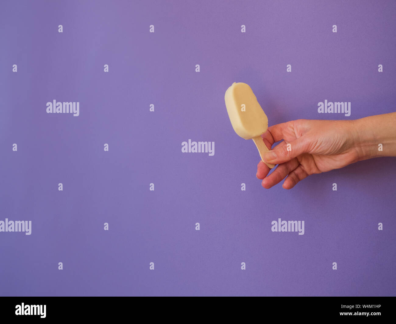 Mano con il cioccolato bianco lollipop icecream su sfondo viola con spazio di copia Foto Stock