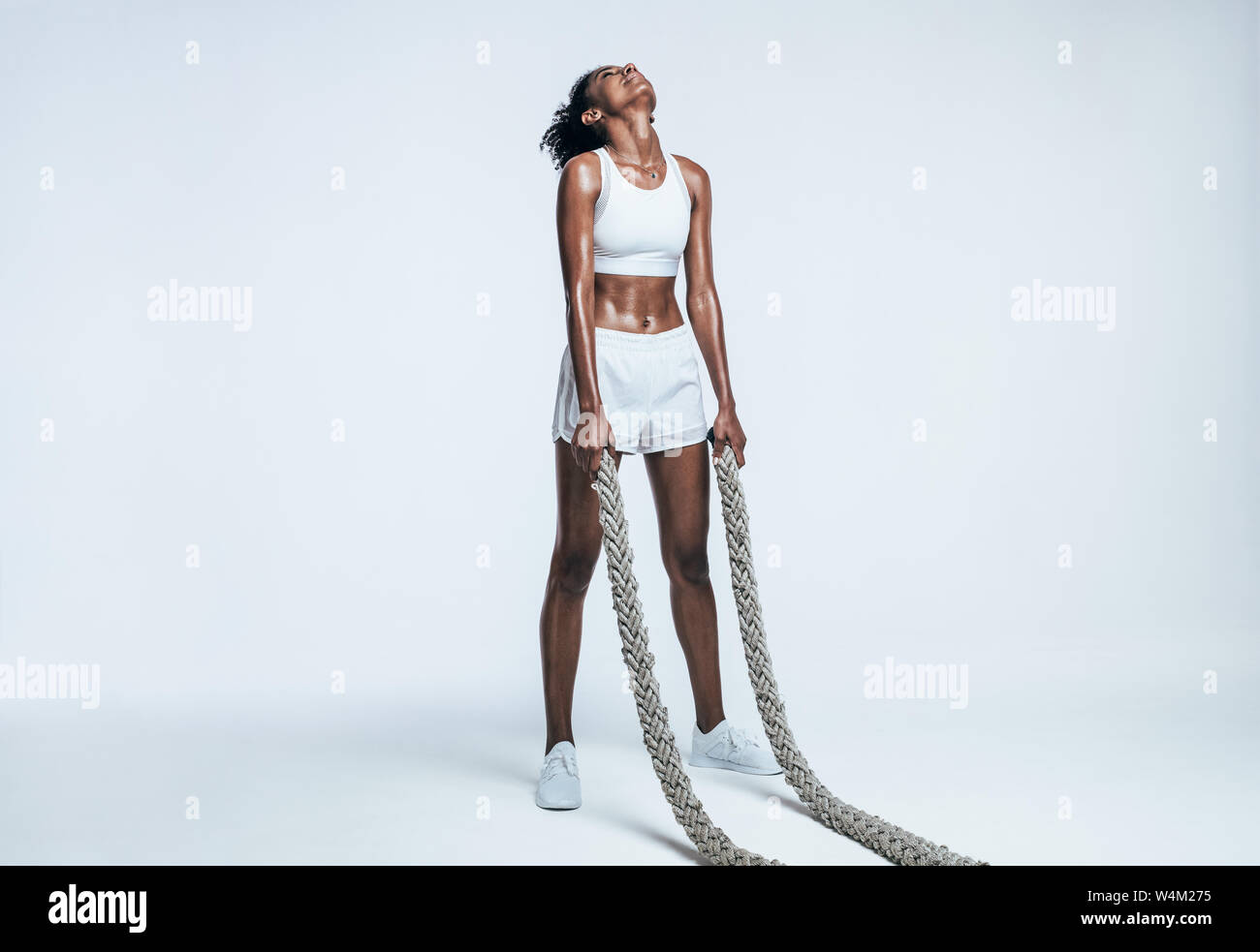 Giovane donna facendo forza di formazione utilizzando corde di battaglia su sfondo bianco. Atleta prendendo una pausa da un intenso allenamento. Foto Stock