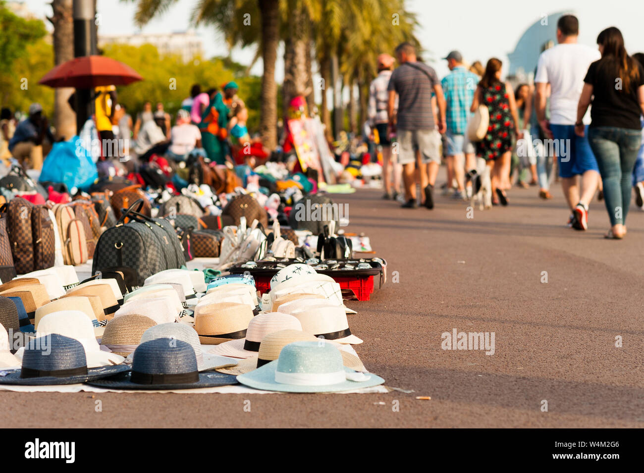 Migranti africani ambulanti denominata 'manteros' vendere merci contraffatte lungo il marciapiede al tramonto con turisti passeggiate per il porto di Barcellona Foto Stock