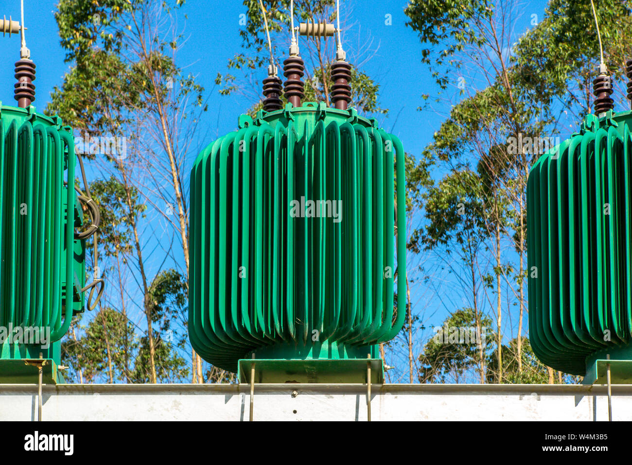 Verde tre trasformatori di energia in calcestruzzo struttura elettrica, con diversi cavi, alberi e cielo blu in background Foto Stock