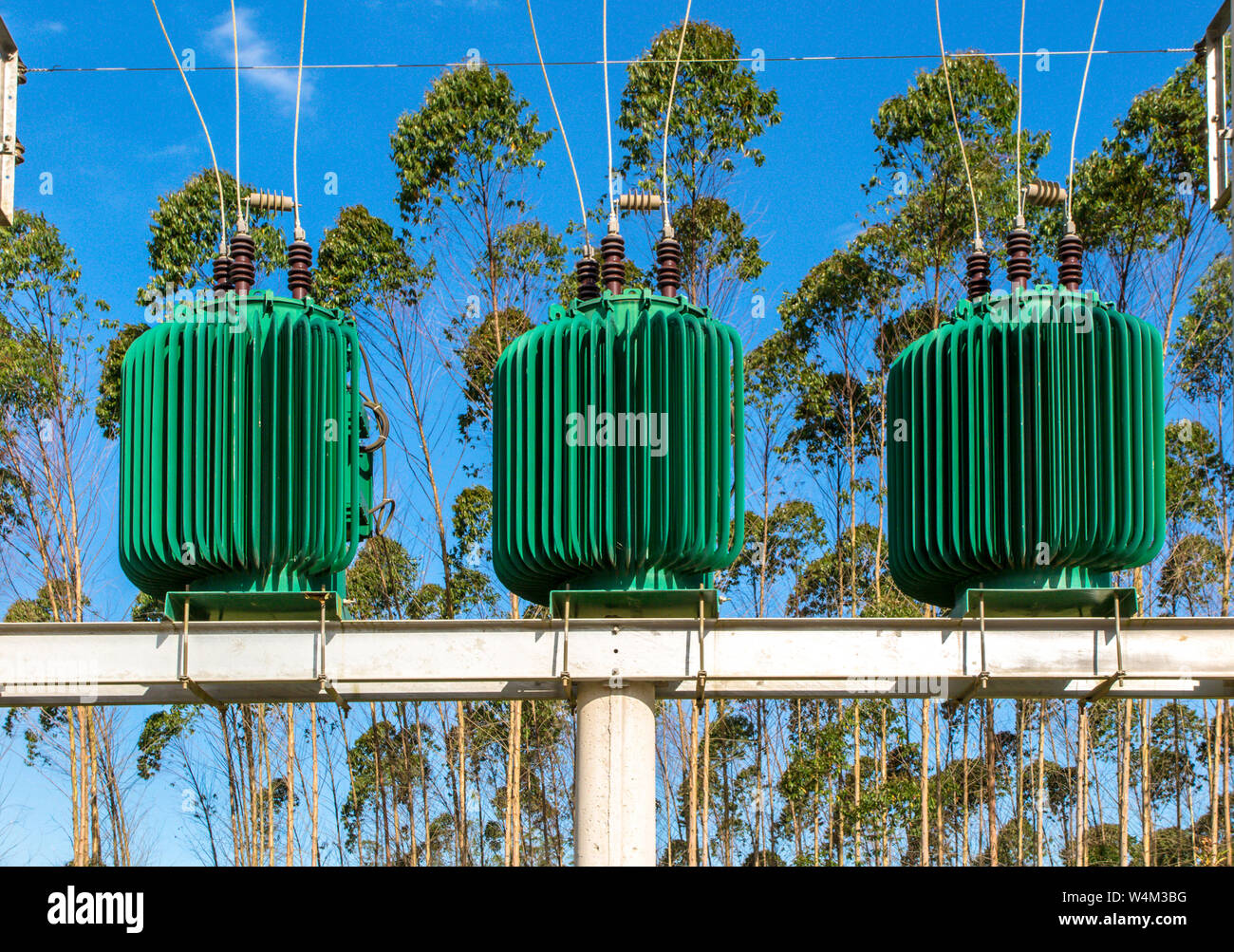 Verde tre trasformatori di energia in calcestruzzo struttura elettrica, con diversi cavi, alberi e cielo blu in background Foto Stock