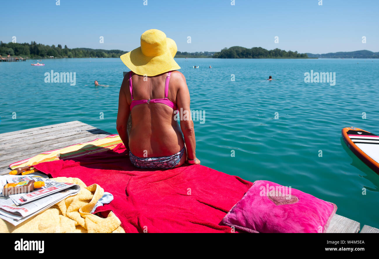 24 luglio 2019, il Land della Baviera, Inning: una donna con un cappello per il sole e bikini si siede nel sole caldo su un molo al worthsee. Foto: Sven Hoppe/dpa Foto Stock