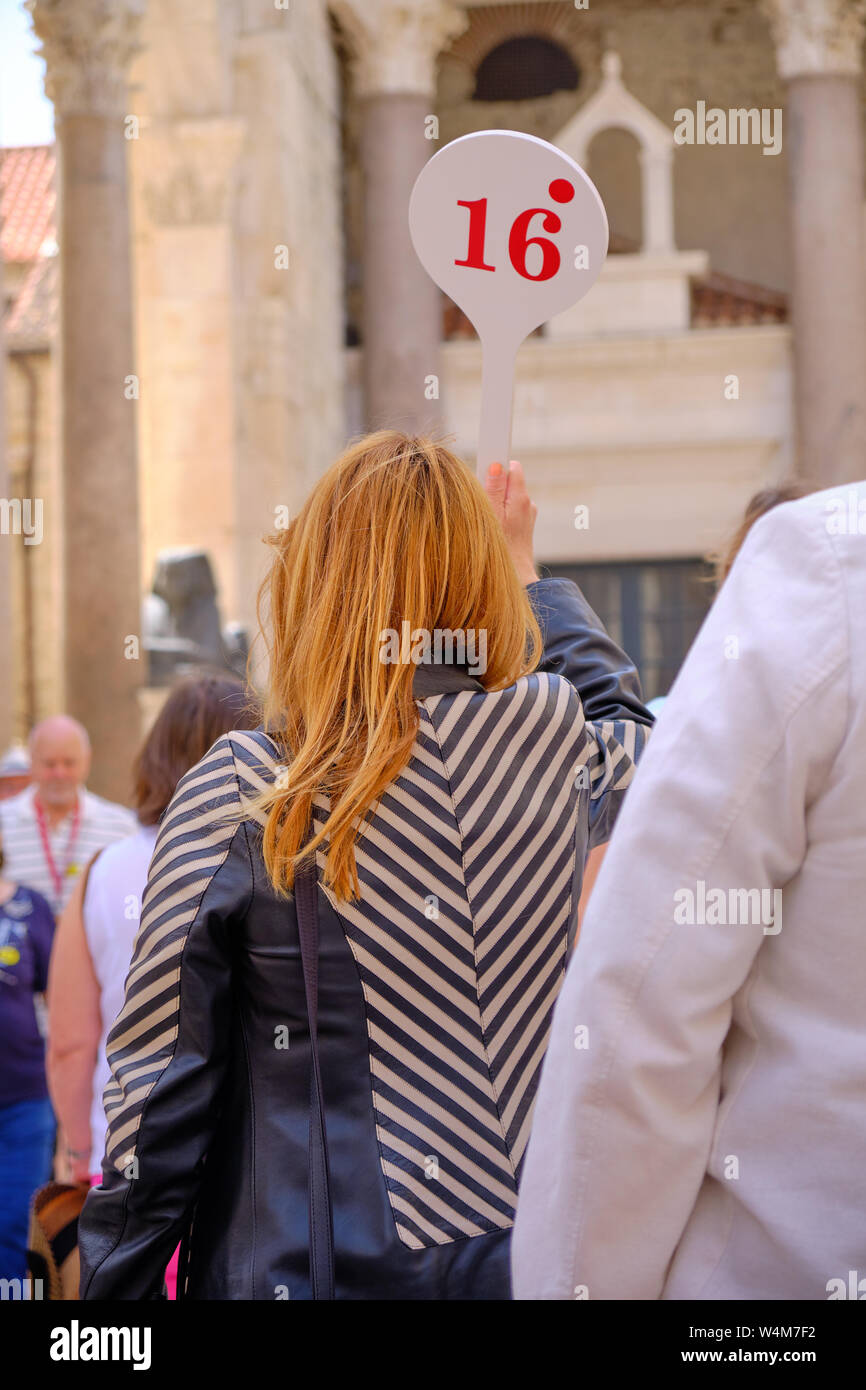 Donna Tour guida visto da dietro con un numero di paletta 16 leader di un gruppo di turisti attraverso la vecchia città europea Foto Stock