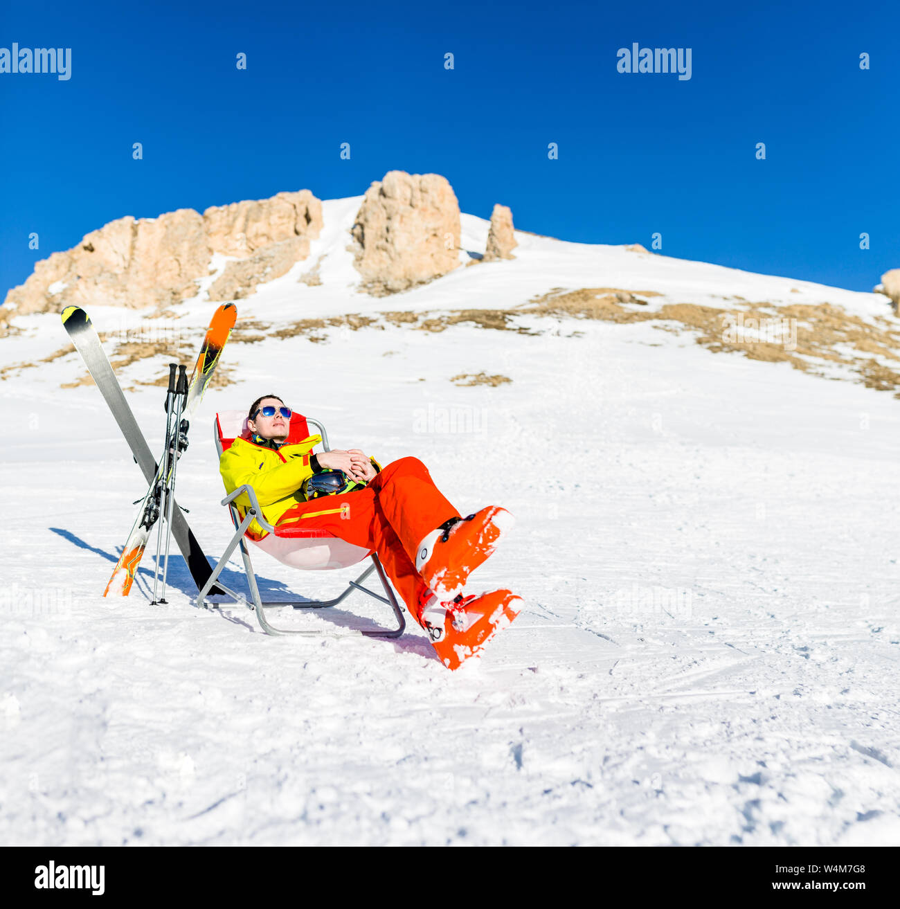 Immagine di sport uomo seduto sulla sedia accanto a sci e bastoni sullo sfondo di montagne innevate Foto Stock