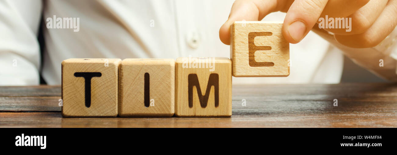 Un uomo mette i blocchi di legno con il tempo di parola. Concetto di gestione del tempo e la distribuzione corretta. Attività di pianificazione e di lavoro. Business della gioventù. Analisi Foto Stock