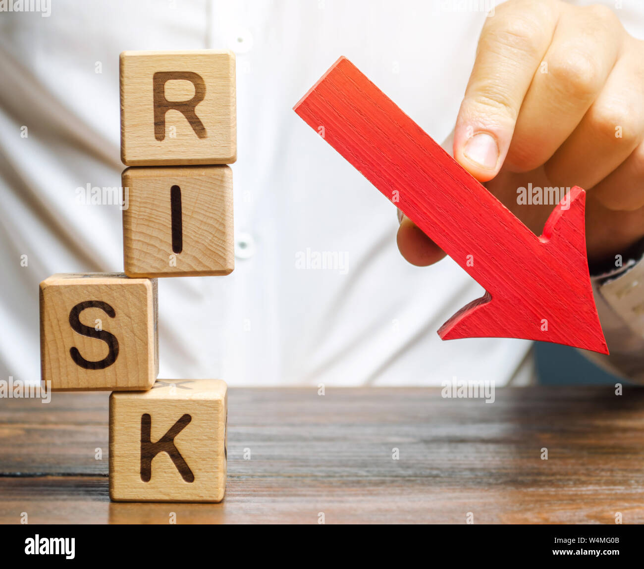 Blocchi di legno con la parola rischio e una freccia giù. Ridurre il rischio finanziario per gli investimenti di capitale e. Protezione dei fondi di investimento e di beni. Anticipo Foto Stock