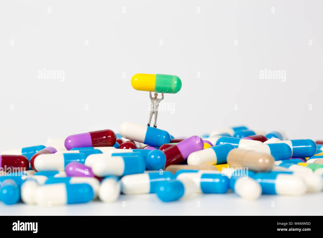 Mucchio di pillole di medicina con la gente in miniatura su sfondo bianco Foto Stock