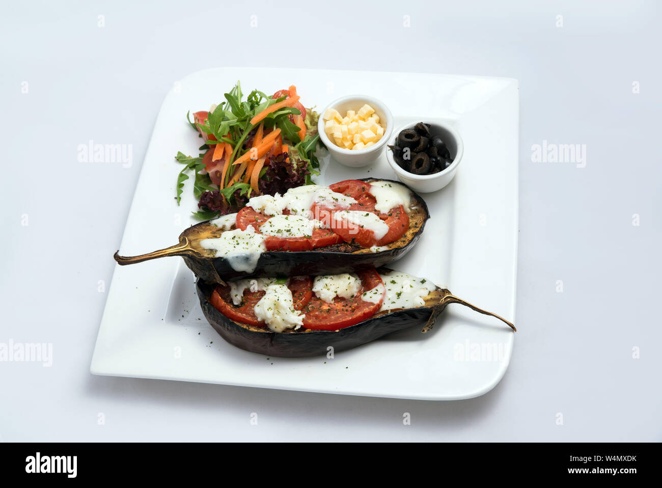 Un basso contrasto eroe caldo colpo di un corso principale piatto con melanzane grigliate con mozzarella di bufala, pomodori, olive e verdure sul lato su un minim Foto Stock