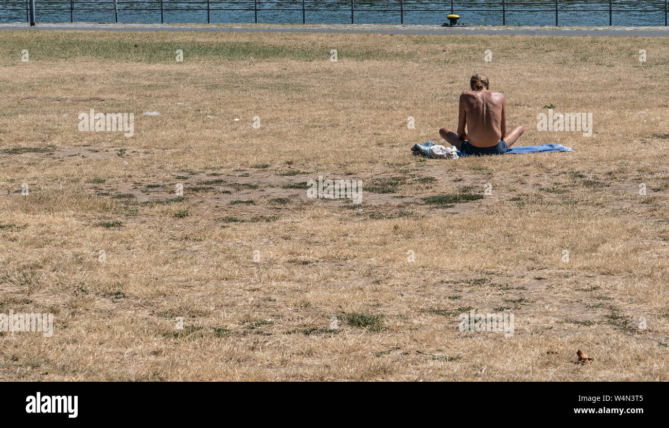 24 luglio 2019, Assia, Frankfurt/Main: un uomo si siede nella calura estiva su un prato appassiti sulle rive del fiume Main. Foto: Frank Rumpenhorst/dpa Foto Stock