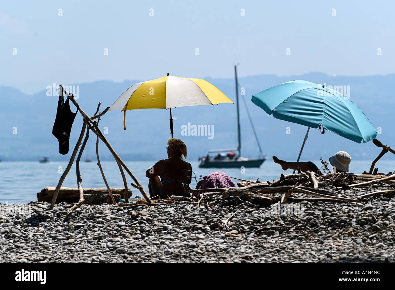 24 luglio 2019, Baden-Wuerttemberg, Gohren am Bodensee: due donne siedono sulla riva del lago di Costanza sotto gli ombrelloni, mentre una barca in background. Foto: Felix Kästle/dpa Foto Stock