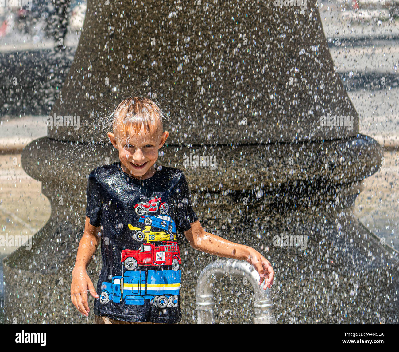 24 luglio 2019, Assia, Frankfurt/Main: sei-anno-vecchio Artem sorge nell'estate calore sotto la fontana presso la Alte Oper e viene irrorato off dall'acqua fredda. Foto: Frank Rumpenhorst/dpa Foto Stock