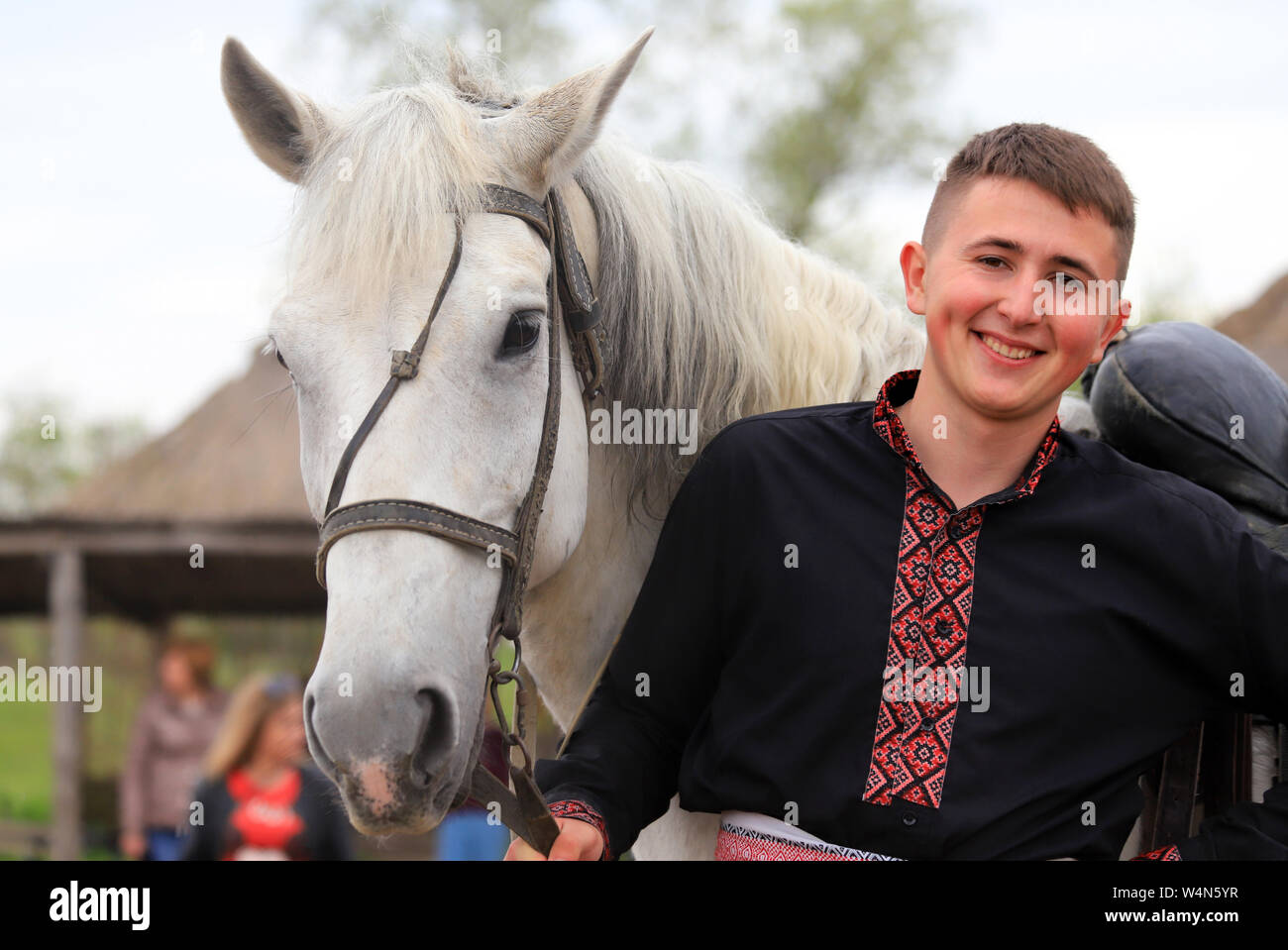 Petrikovka, Dnepropetrovsk regione, Ucraina, 28 04 2019 un giovane uomo ucraino, cosacco in camicia ricamata sorrisi e trattiene un cavallo grigio, etnico festi Foto Stock