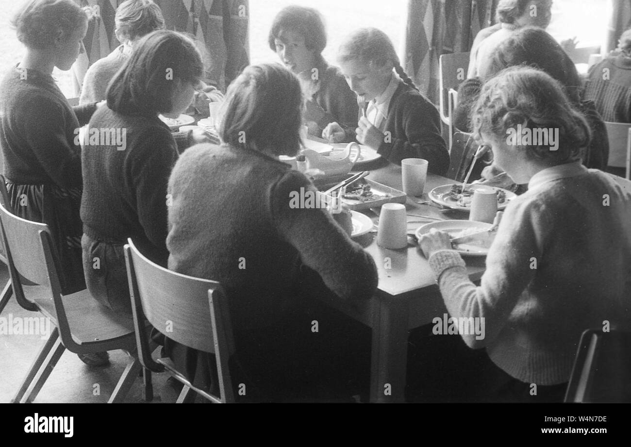 Degli anni Cinquanta, storico, un gruppo di studentesse in una contea di scuola secondaria seduti insieme ad un tavolo avente il pranzo, Inghilterra, Regno Unito. Foto Stock