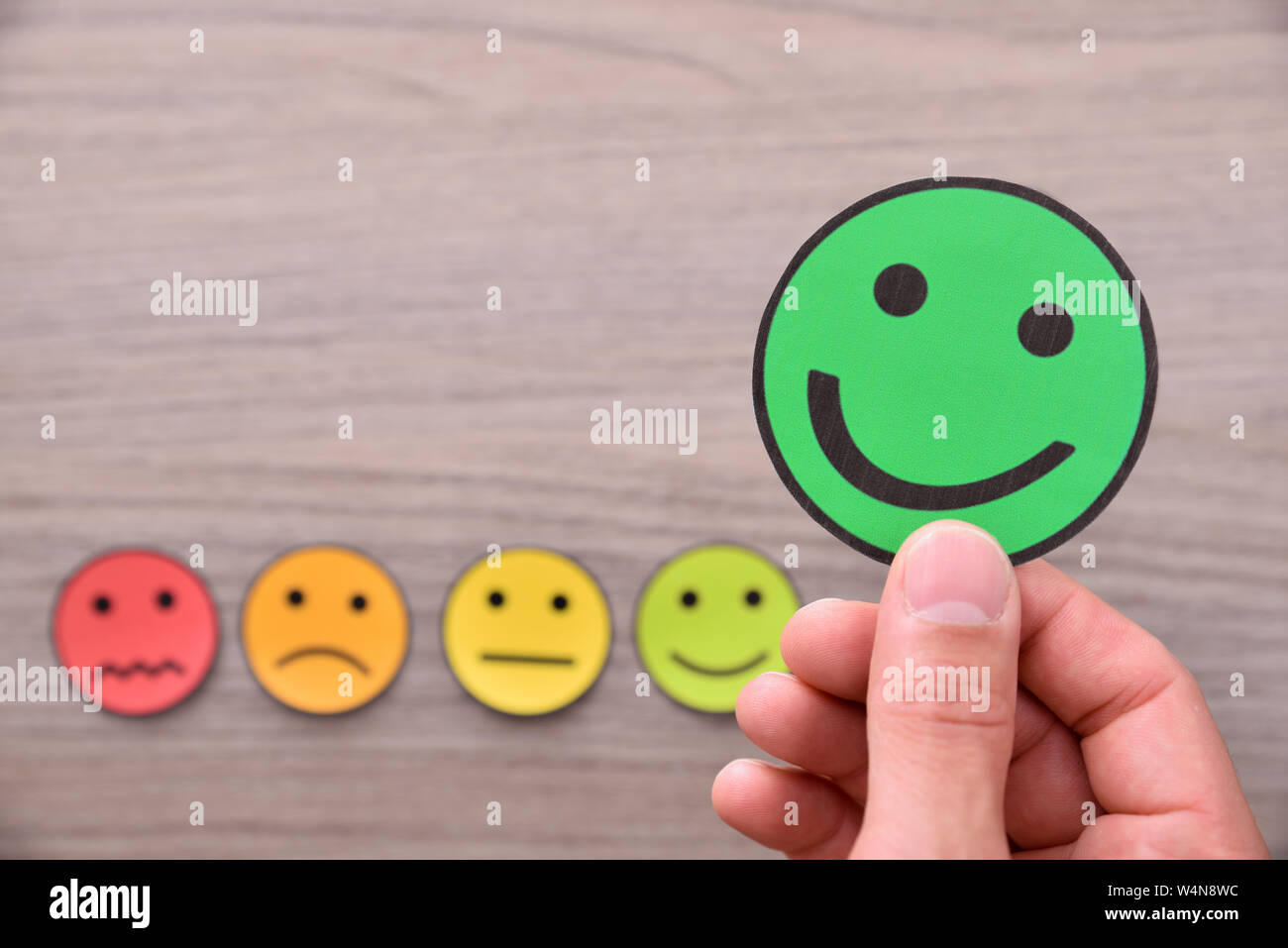 Mano tenendo una valutazione positiva rappresentata con ritagli di faccia con espressioni diverse. Composizione orizzontale. Vista dall'alto. Foto Stock