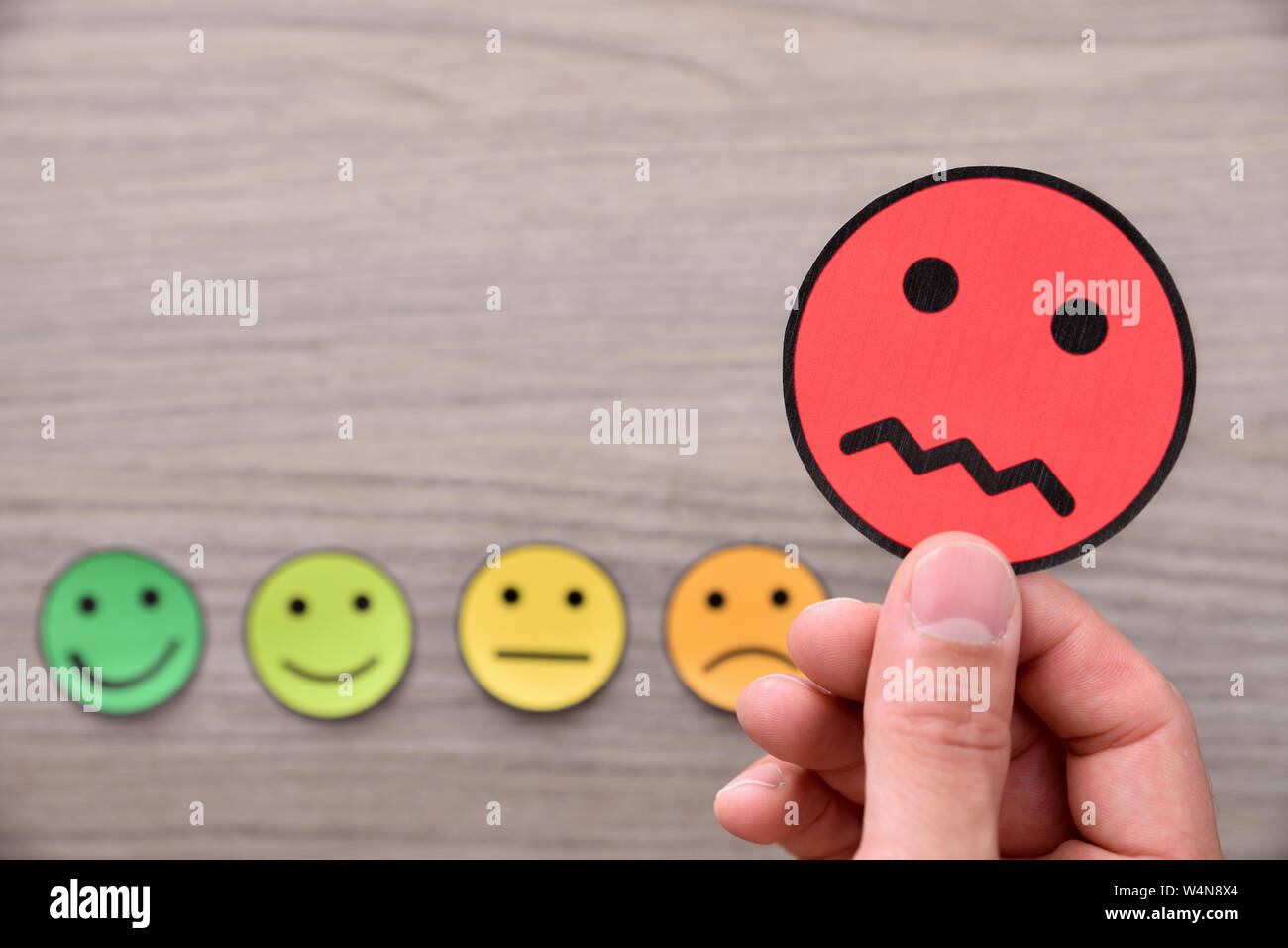 Mano tenendo una valutazione negativa rappresentata con ritagli di faccia con espressioni diverse. Composizione orizzontale. Vista dall'alto. Foto Stock