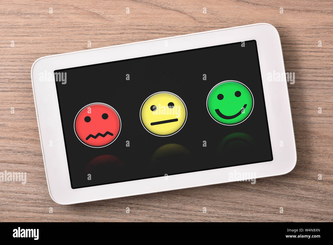 Soddisfazione dei livelli di rappresentazione con le emoticon sul tablet nero schermo sul tavolo di legno vicino. Composizione orizzontale. Vista dall'alto. Foto Stock