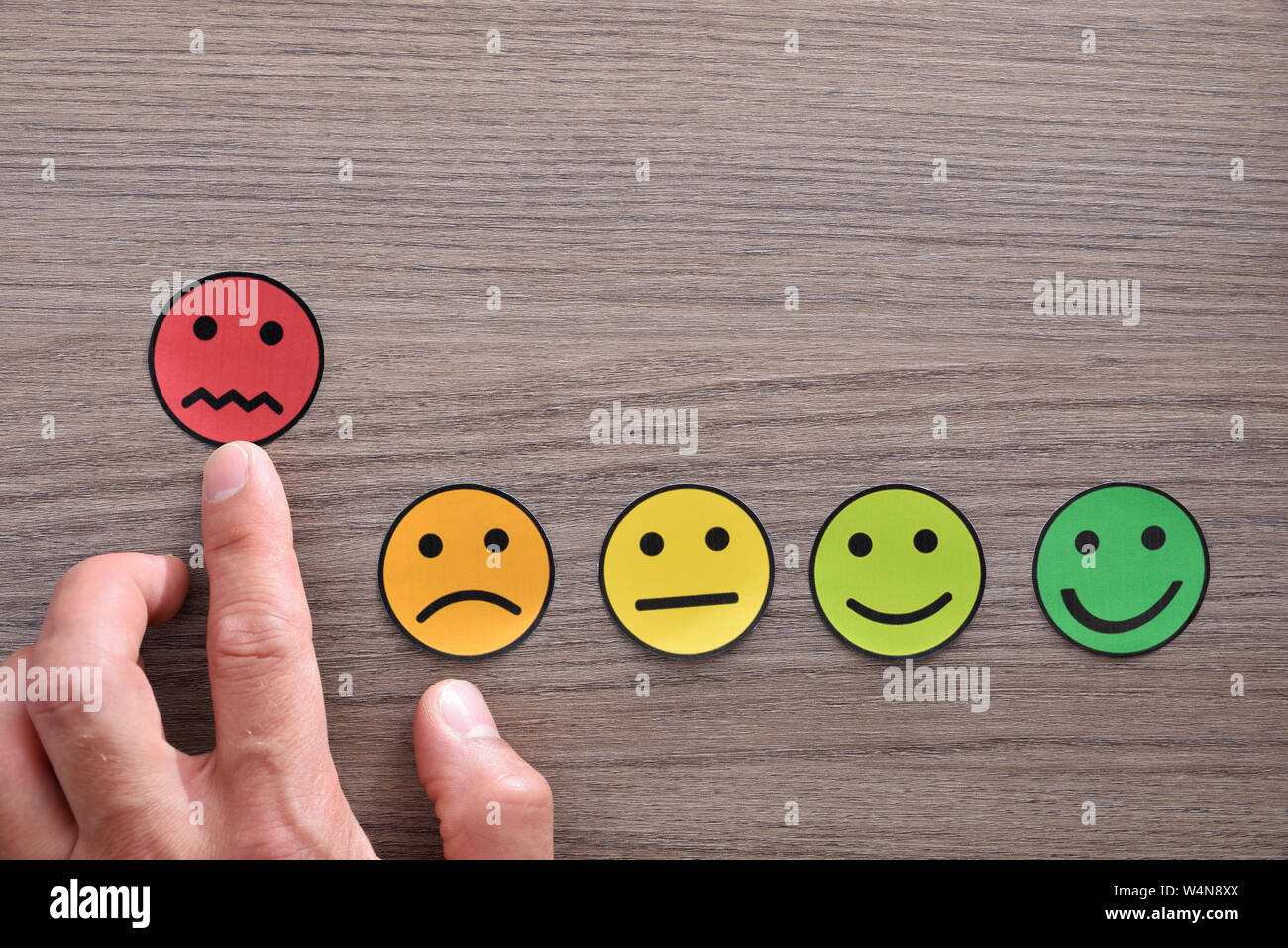 Puntamento a mano un livello di soddisfazione negativa rappresentata con le emoticon colorate sul tavolo di legno. Composizione orizzontale. Vista dall'alto. Foto Stock