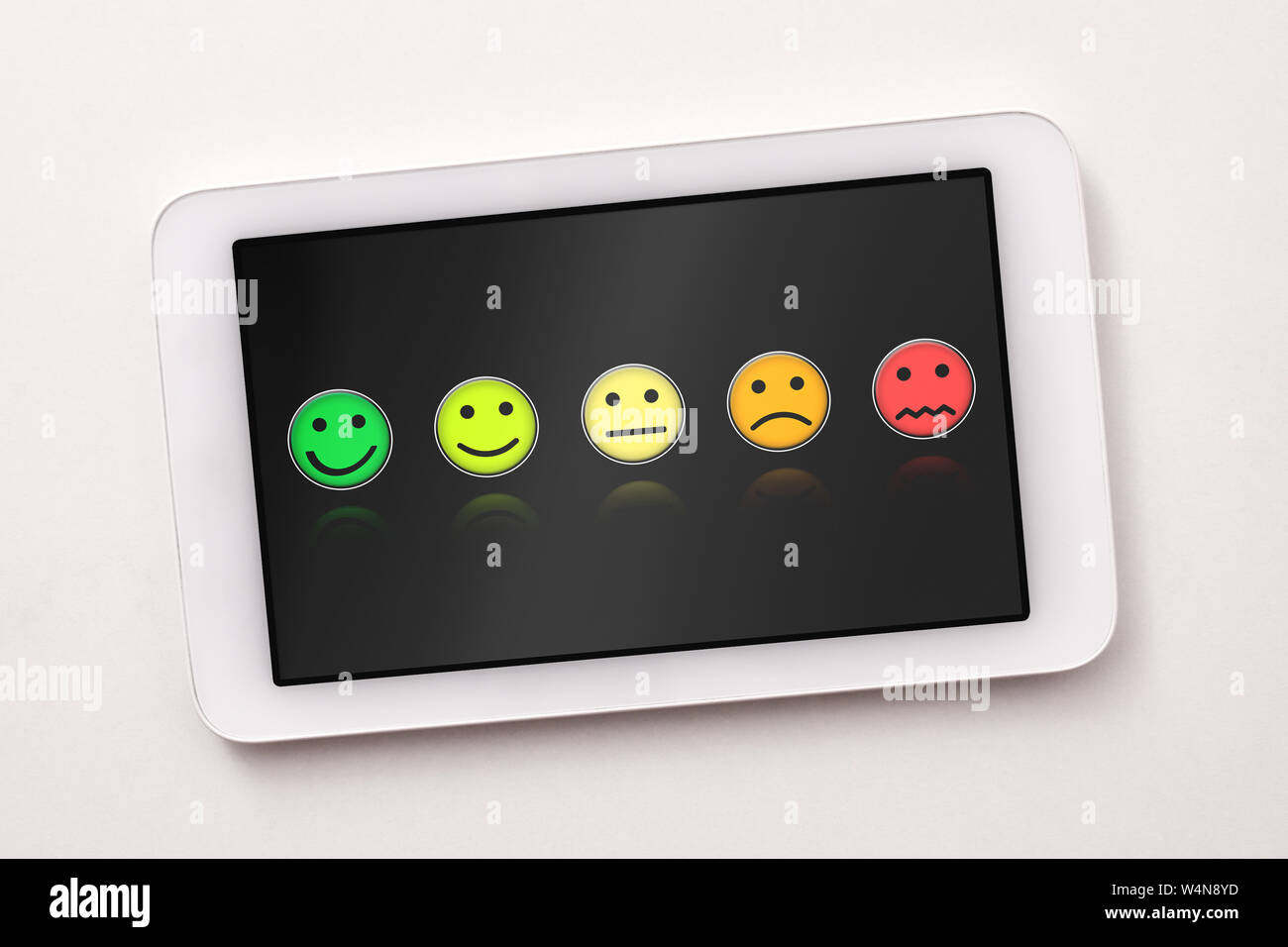 Soddisfazione dei livelli di rappresentazione con le emoticon sulla schermata blacktablet sul tavolo bianco vicino. Composizione orizzontale. Vista dall'alto. Foto Stock