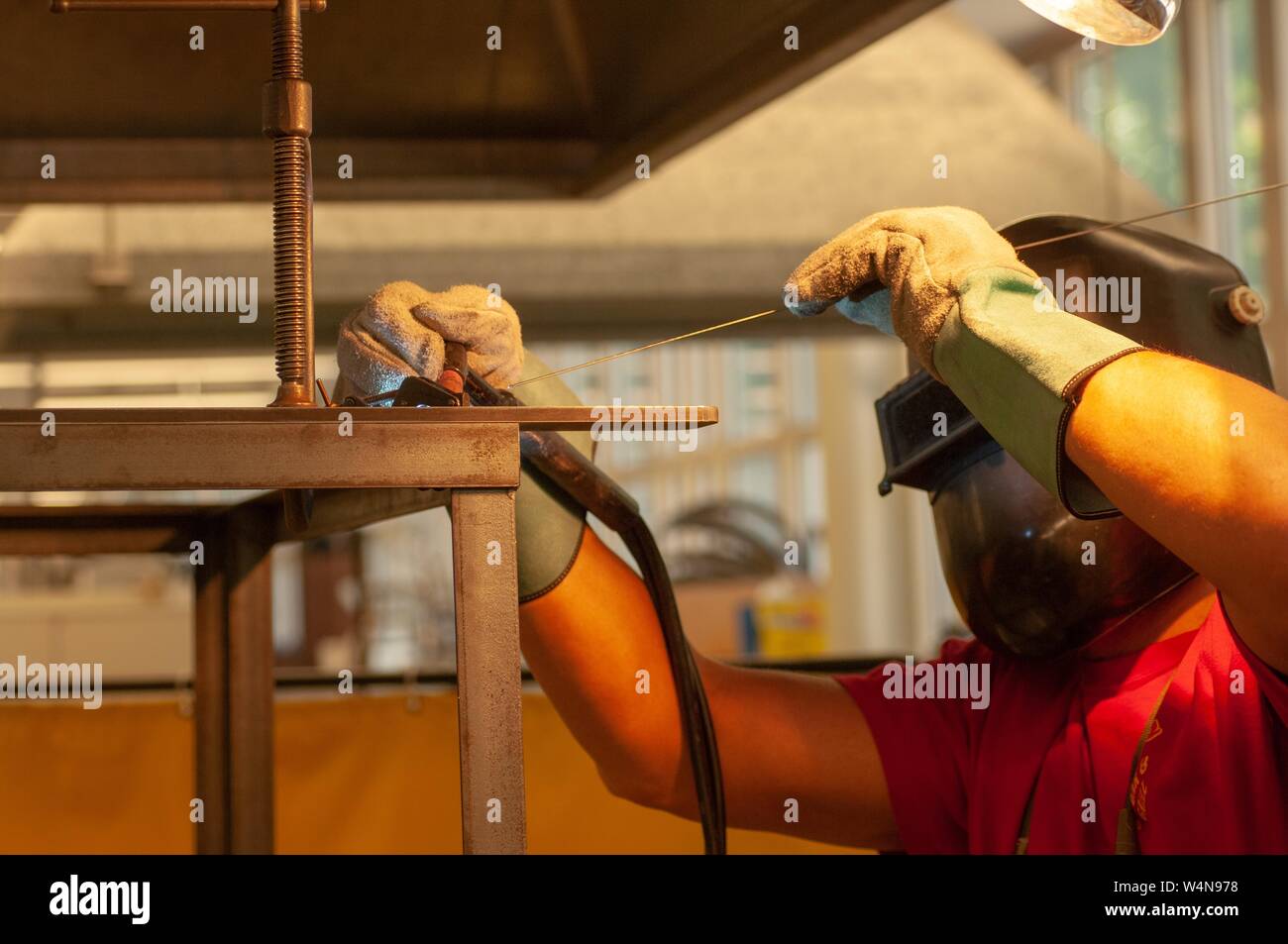 Visualizzazione del profilo di un saldatore, indossa un casco di protezione e guanti, lavorando con un'asta in un negozio di macchina presso la Johns Hopkins University, Baltimora, Maryland, Ottobre 2, 2006. Dall'Homewood raccolta di fotografie. () Foto Stock