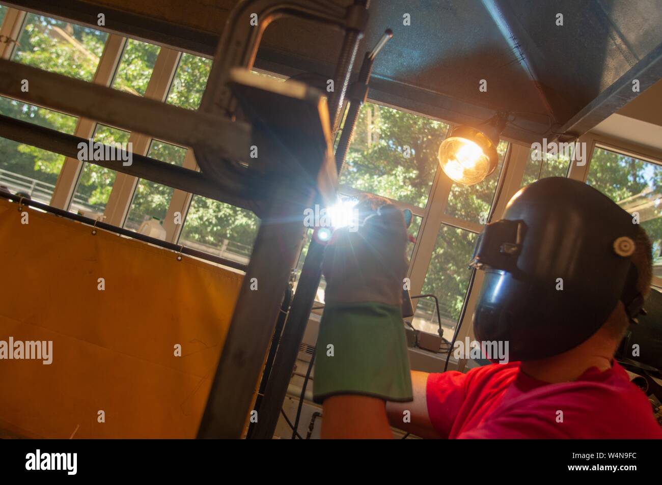 Profilo angolato tiro di una saldatrice, che indossa un casco di protezione e guanti, lavora in un negozio di macchina presso la Johns Hopkins University, Baltimora, Maryland, Ottobre 2, 2006. Dall'Homewood raccolta di fotografie. () Foto Stock