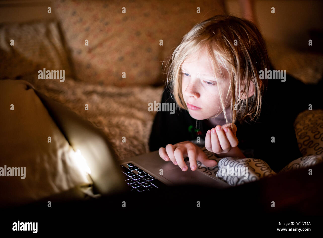 Giovane ragazzo a letto con il computer portatile Foto Stock
