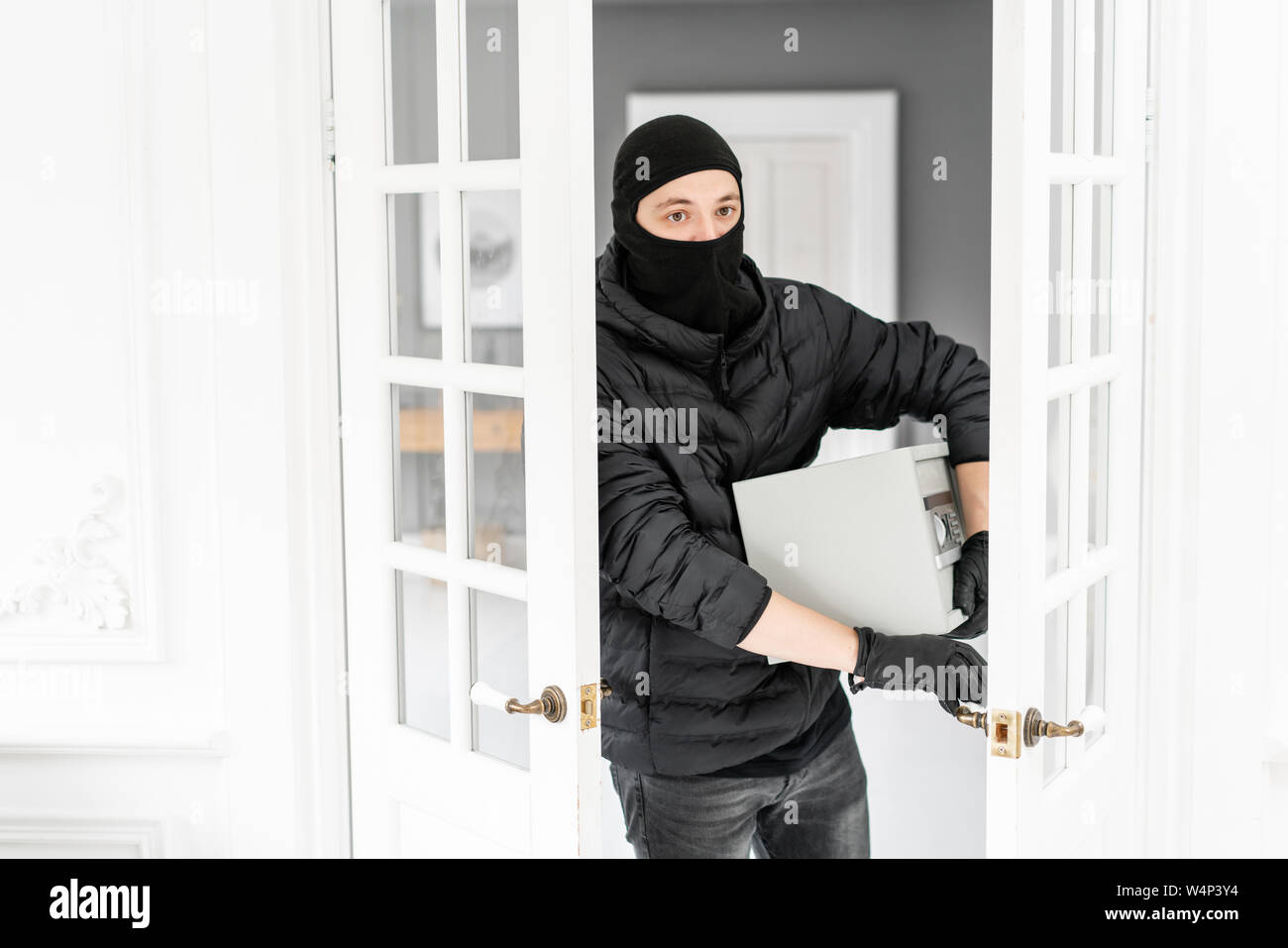 Il ladro commette un reato in un appartamento di lusso con stucco. Ladro con nero balaclava rubare moderno cassetta di sicurezza elettronica. Foto Stock
