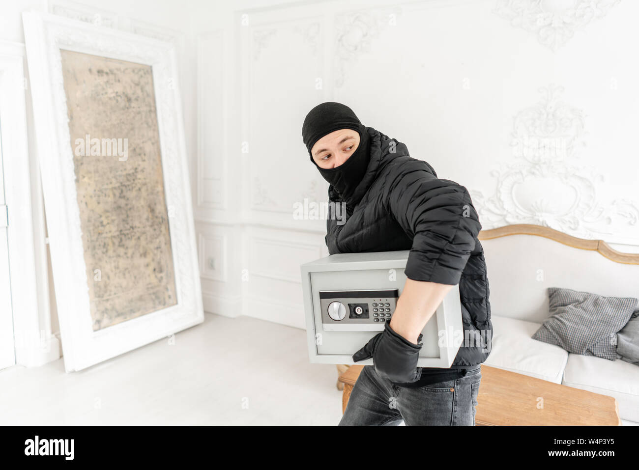 Ladro con nero balaclava rubare moderno cassetta di sicurezza elettronica. Il ladro commette un reato in un appartamento di lusso con stucco. Foto Stock