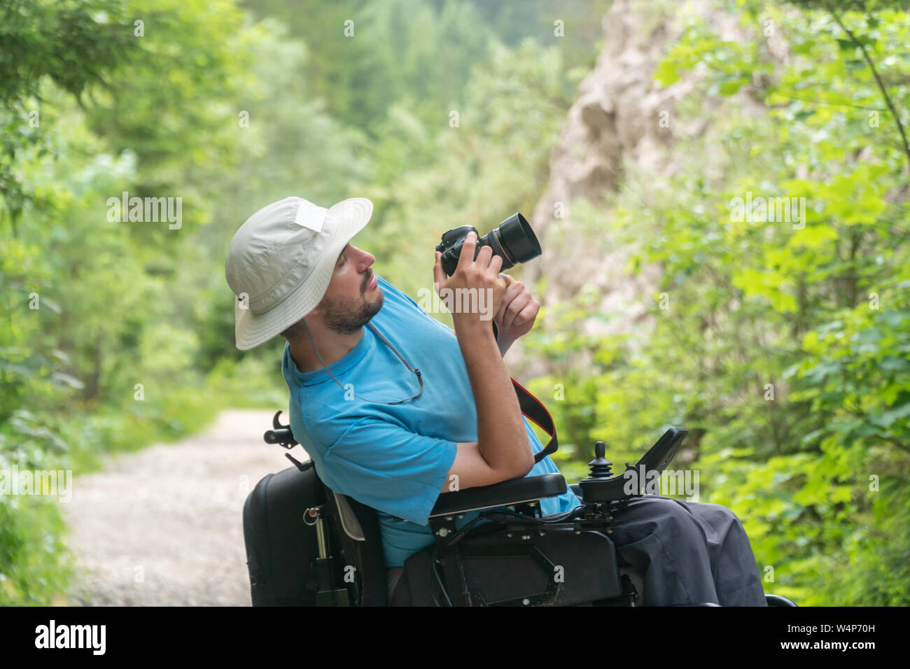 Uomo sulla sedia elettrica utilizzando la fotocamera mirrorless natura, godere di libertà e di fare arte Foto Stock