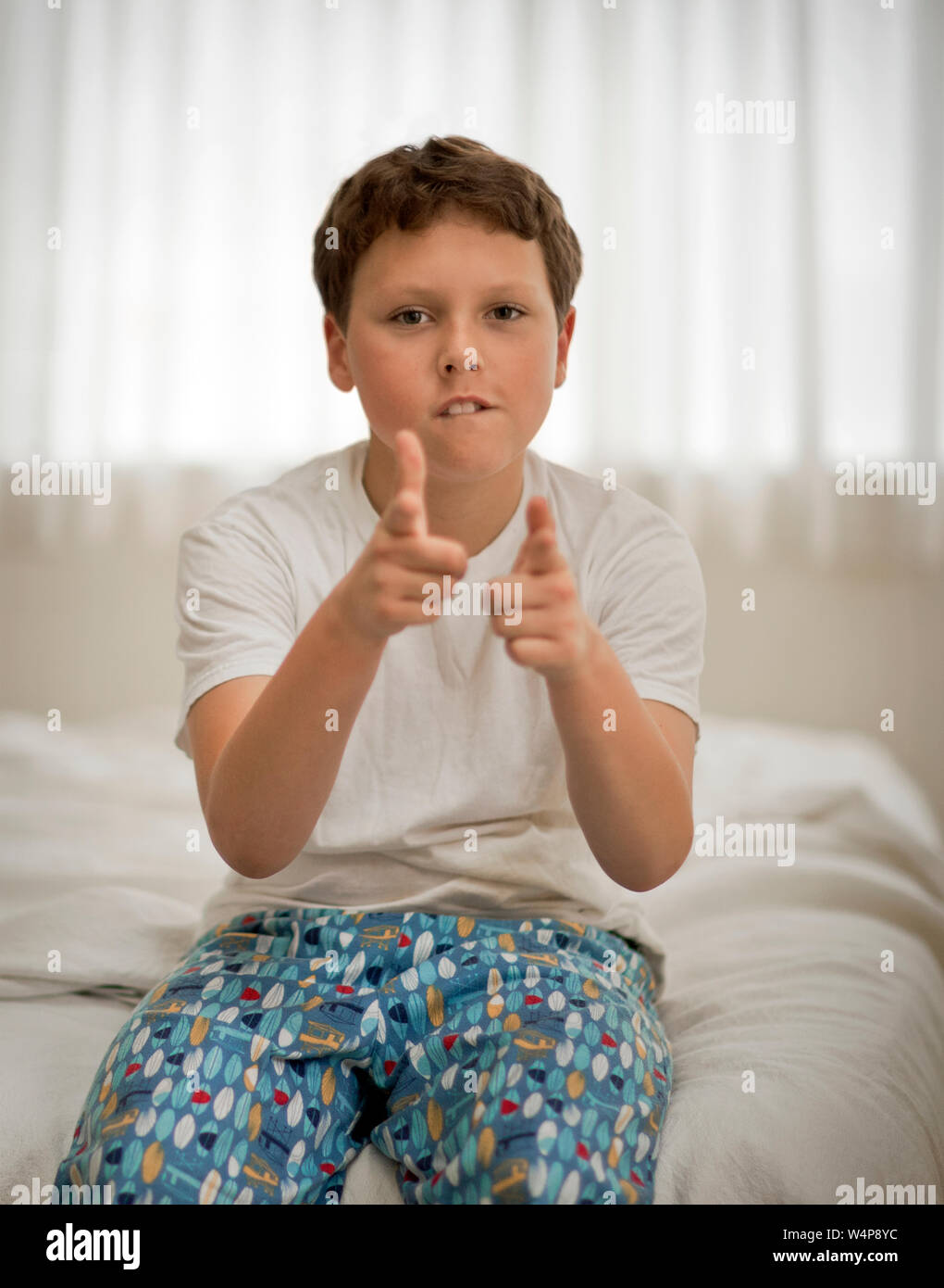 Preteen boy indossando pigiami punti un dito pistola alla telecamera. Foto Stock