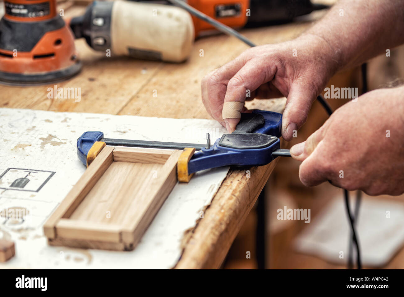 Close-up carpentiere senior incollaggio di artigianato in legno e superficie di raccordo con le fascette. Opere in legno falegname con attrezzature e utensili in officina. Fai da te fatti a mano Foto Stock