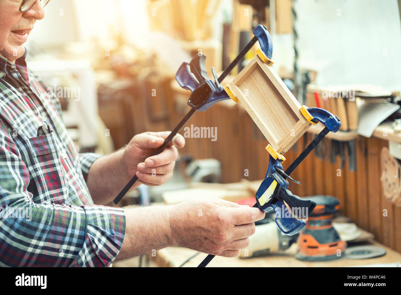 Senior falegname incollaggio di artigianato in legno e superficie di raccordo con le fascette. Opere in legno falegname con attrezzature e utensili in officina. Fatte a mano mobili fai da te Foto Stock