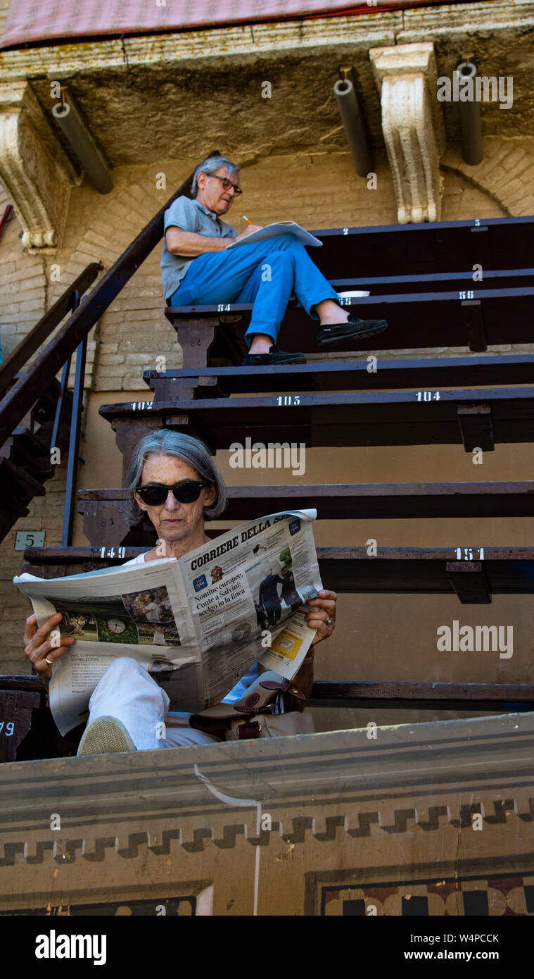 L uomo e la donna leggere quotidiani in gradinate in Piazza de Campo mentre in attesa di avvio del Palio di Siena, Italia Foto Stock