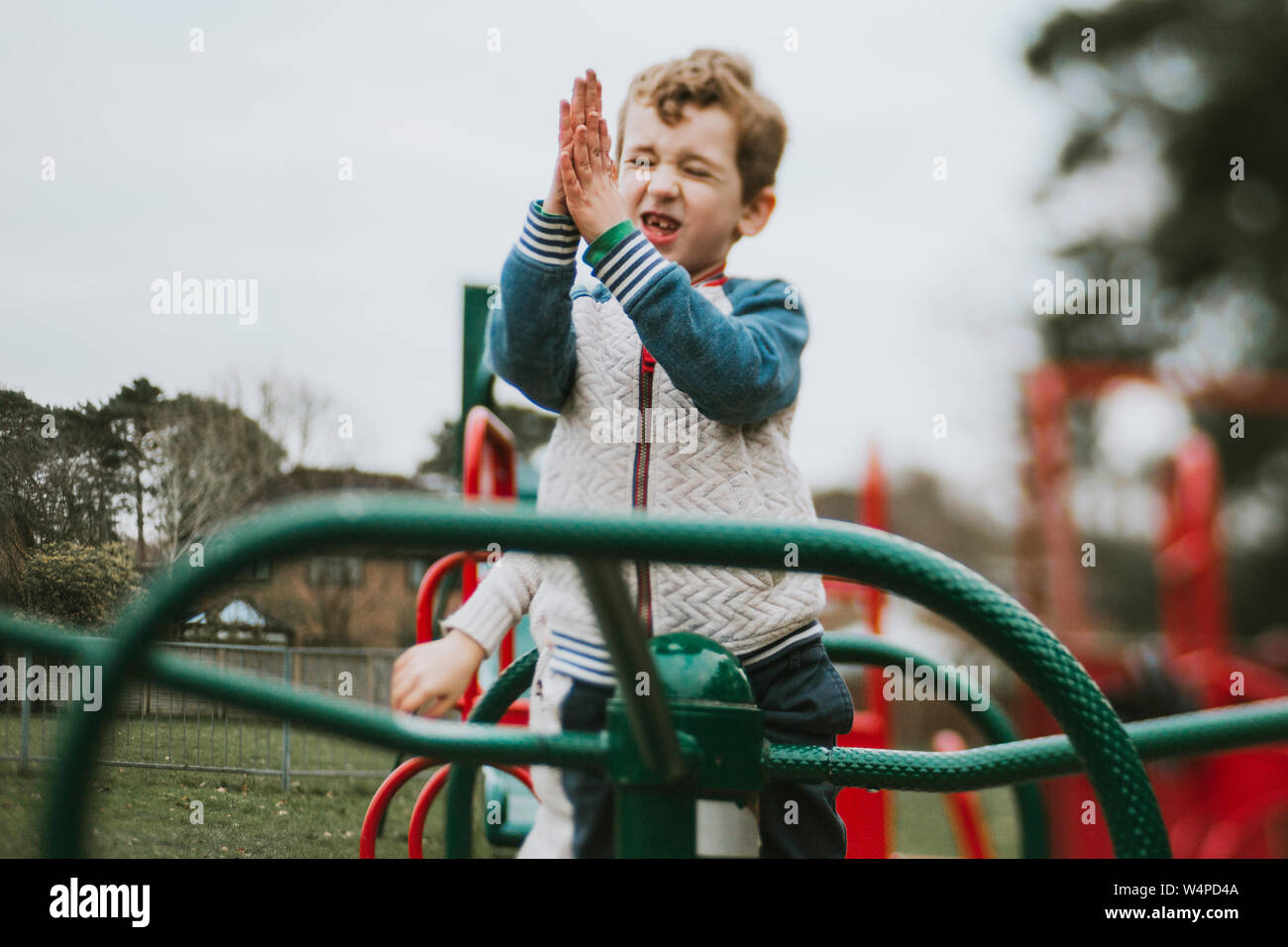 Vista laterale del ragazzo battendo le mani su Merry Go Round al parco giochi Foto Stock