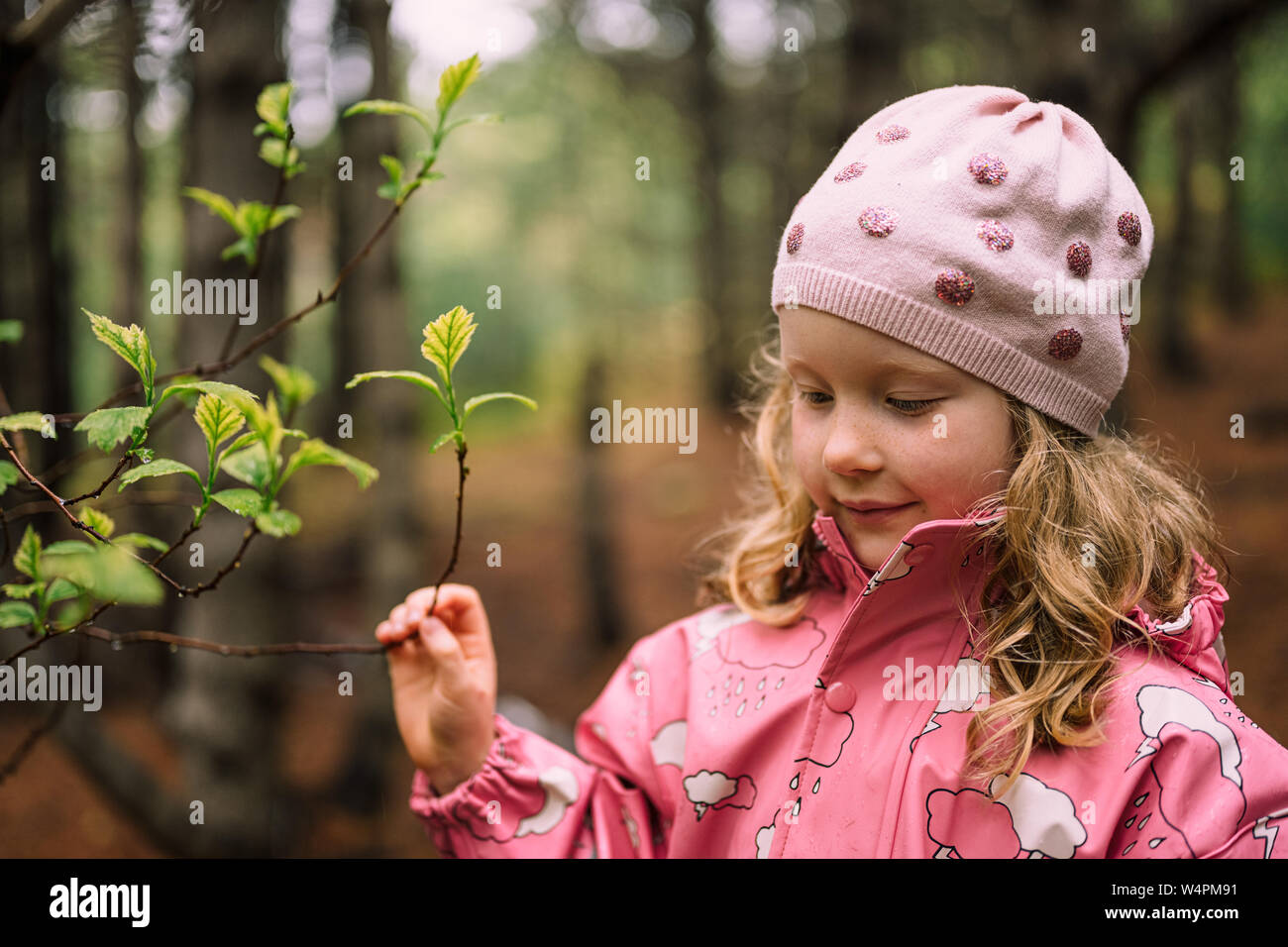 Adorabile ragazza in abiti rosa esaminando il ramo con le foglie nella foresta di Reykjavik, Islanda Foto Stock