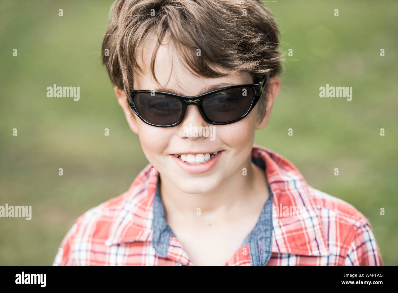 Ragazzo, dieci anni, con occhiali da sole e plaid shirt guardando sorridente, Ritratto, Germania Foto Stock