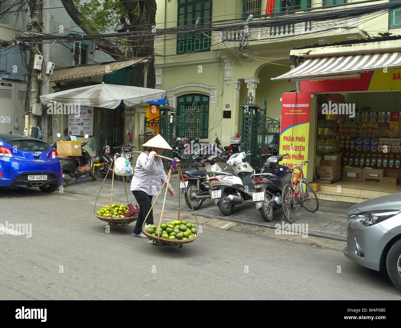 HANOI, VIETNAM - Giugno 28, 2017: una donna che porta frutto usando una spalla pole e due cestelli lungo una strada di Hanoi Foto Stock