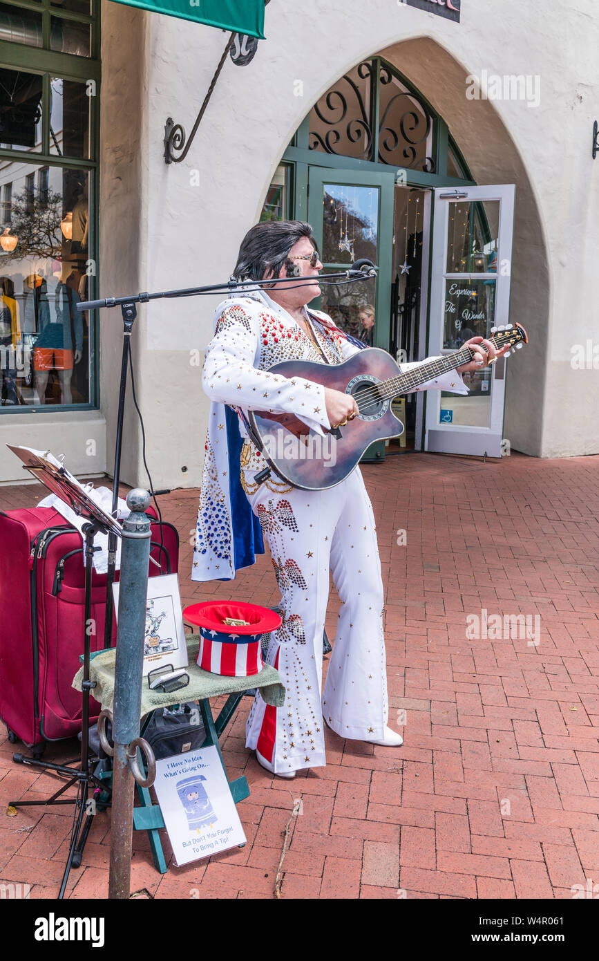 Un Elvis Presley impersonator, vestito di un Elvis come bianco sequined  costume, suona la chitarra e canta con un microfono sul marciapiede davanti  Foto stock - Alamy