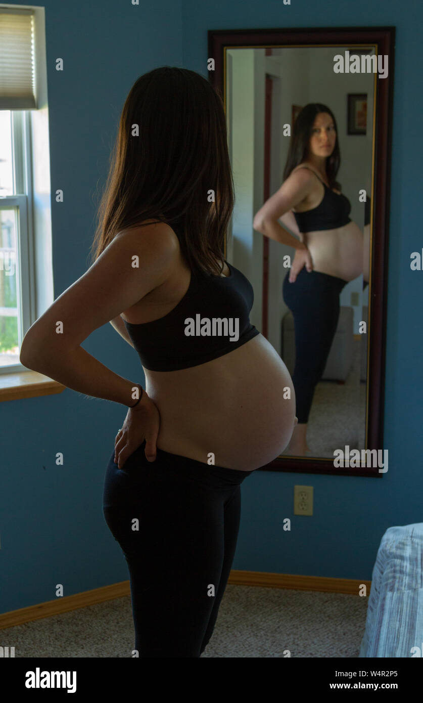 Donna incinta, fine nel terzo trimestre, facendo una curva posteriore di fronte ad uno specchio per alleviare alcuni dei la maggior parte inferiore della schiena dolore causato da bambino. Foto Stock