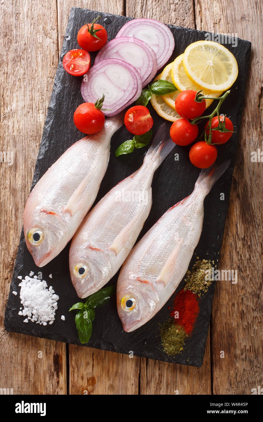 Orata bram di mare Pesce con ingredienti di close-up su una scheda di ardesia sul tavolo. Verticale in alto vista da sopra Foto Stock