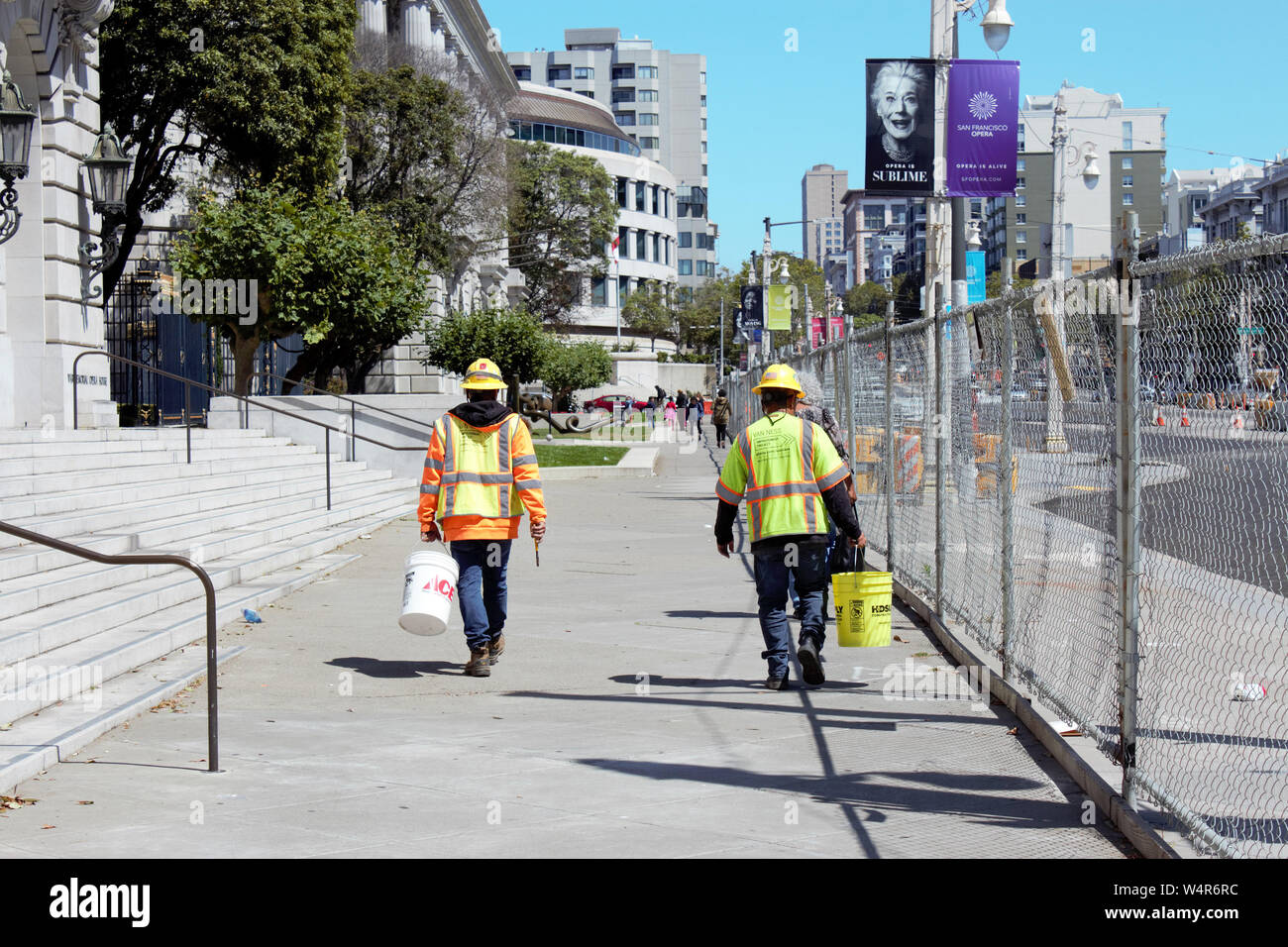 Lavoratori edili che trasportano le benne a piedi lungo il marciapiede accanto a un sito in costruzione. Foto Stock