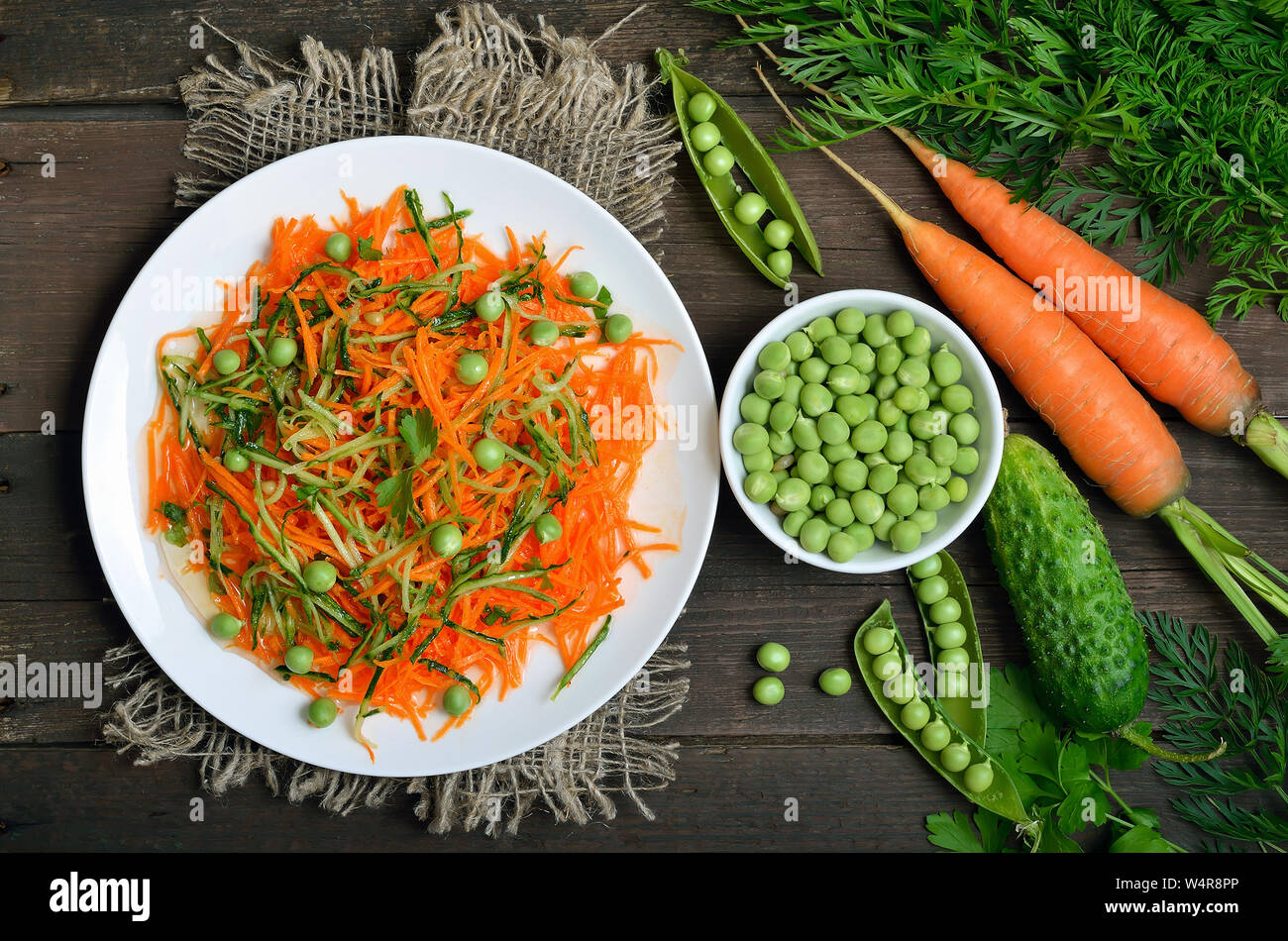 Deliziosa Insalata di carote, cetriolo, pinoli e piselli verdi sulla piastra bianca, vista dall'alto. Ortaggi freschi sul tavolo di legno, vista dall'alto Foto Stock