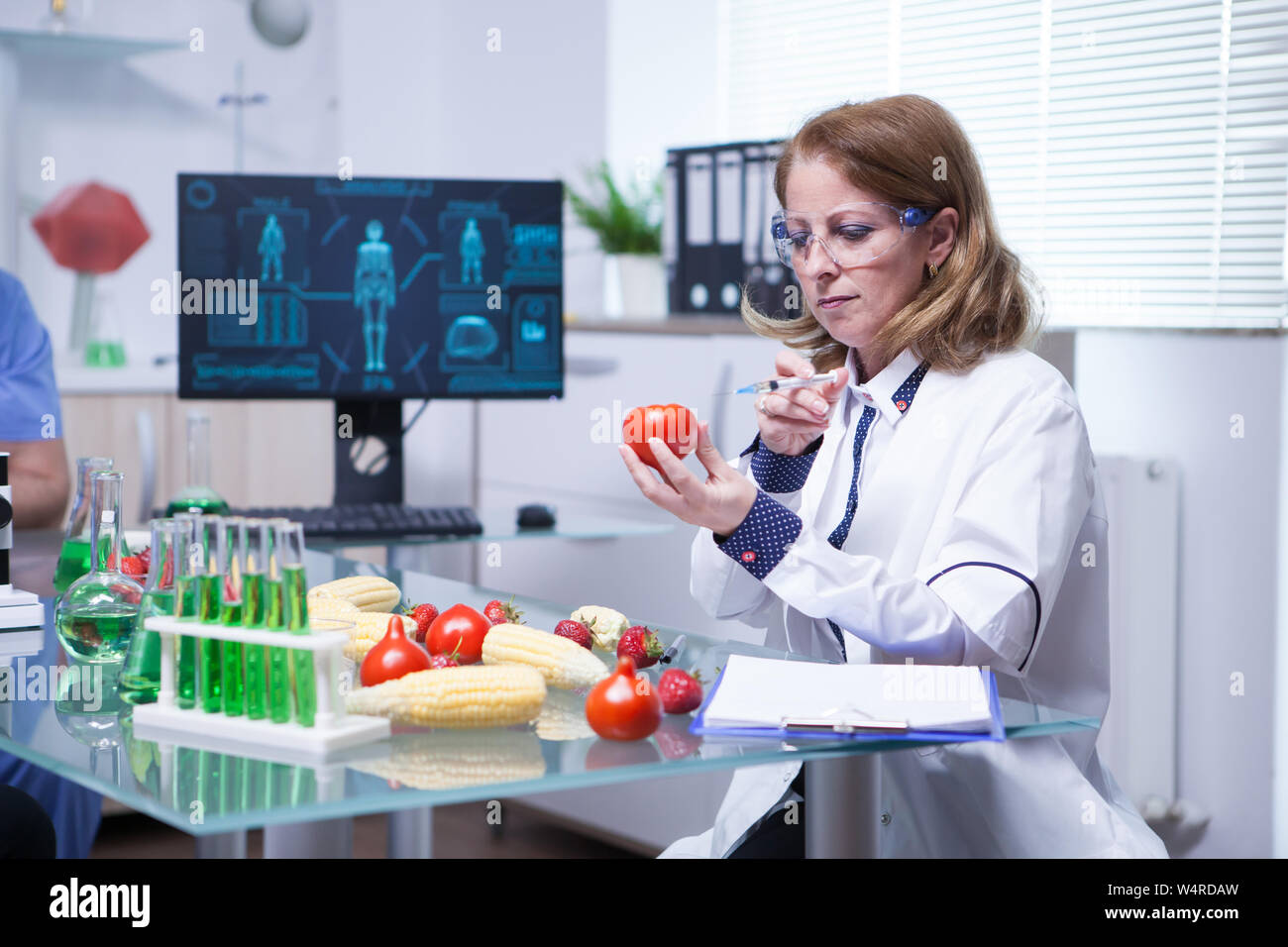 Il biologo in camice bianco in un laboratorio di ricerca iniettare liquido  in un pomodoro. Provette con liquido verde Foto stock - Alamy