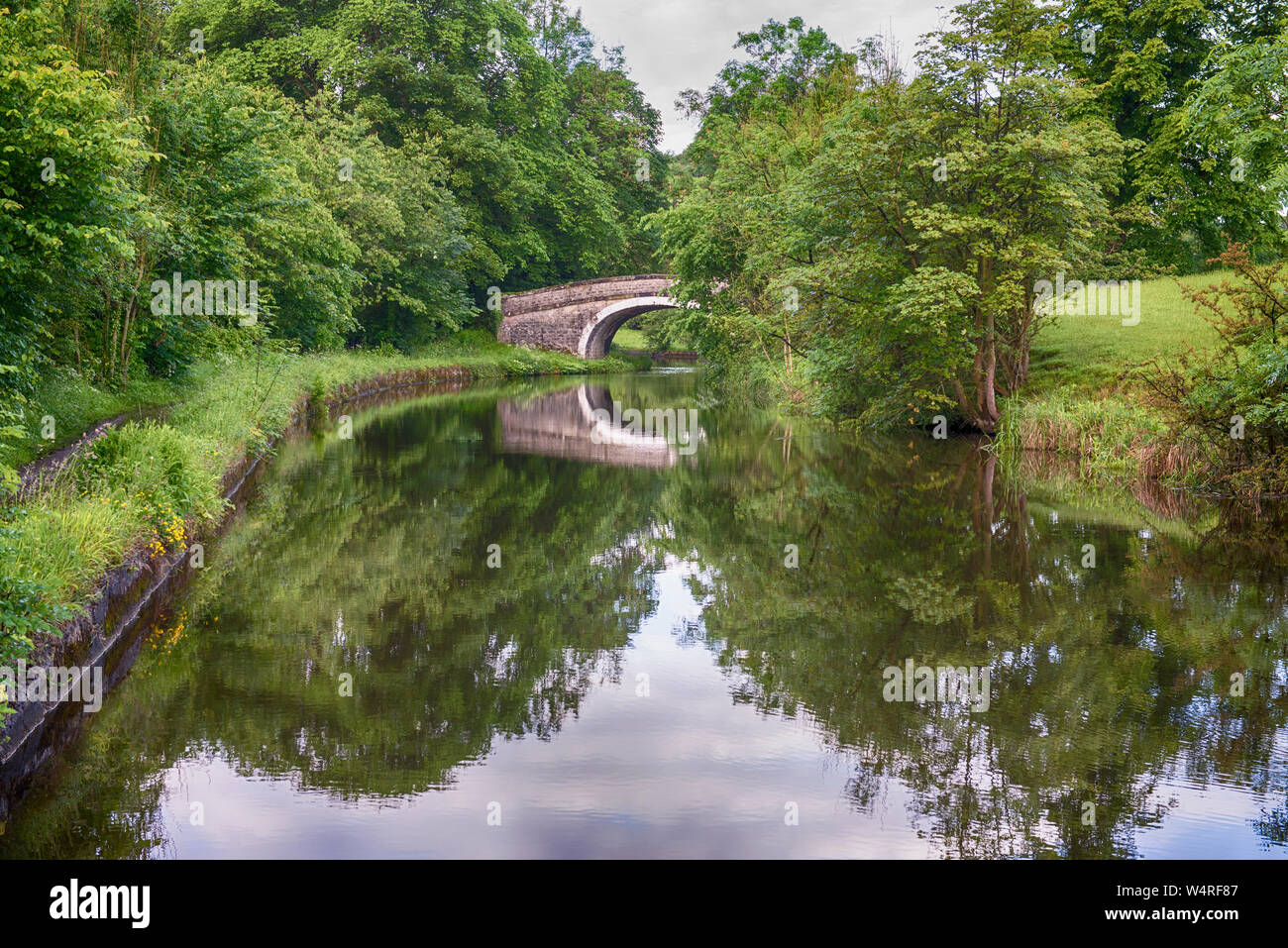 Vista di un inglese un paesaggio rurale paesaggi sulla British canale navigabile durante il giorno nuvoloso con old stone road bridge Foto Stock