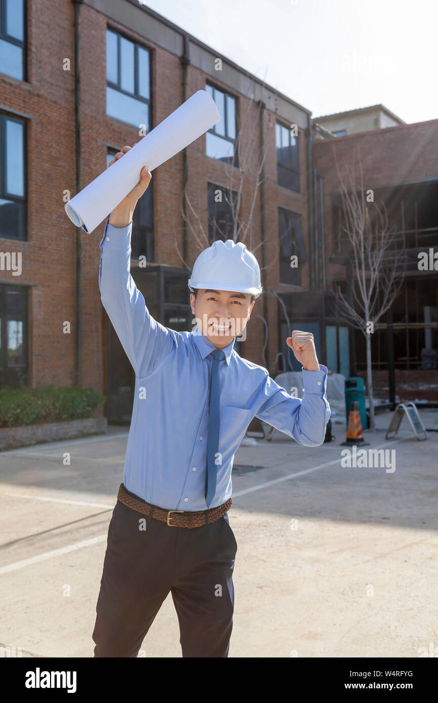 Architetto maschio indossando il casco di sicurezza tenendo blueprint, Pechino, Cina Foto Stock